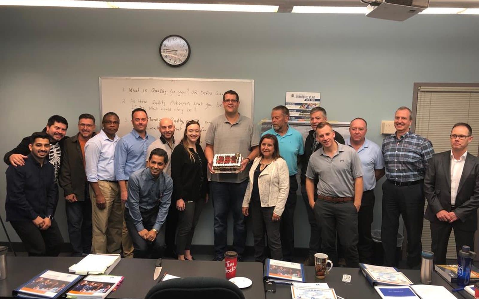 A cohort standing together at the end of a session, the day’s quality-management questions still on the whiteboard behind them.