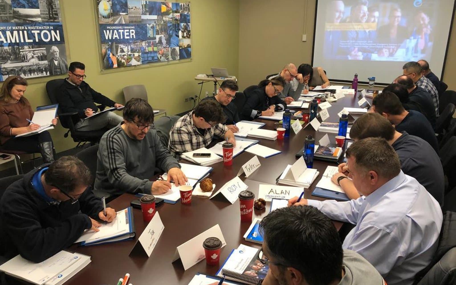 A full boardroom of City of Hamilton staff taking notes during one of our sessions, under the department's water and wastewater signage.