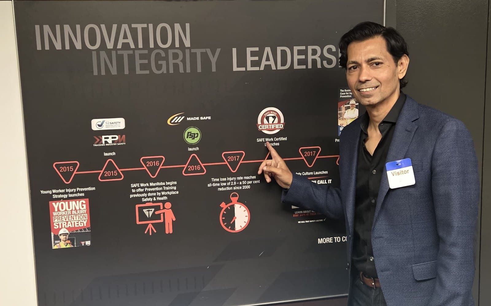 Hemant Dhariyal pointing at a milestone on the SAFE Work Manitoba timeline wall inside the organisation's offices.